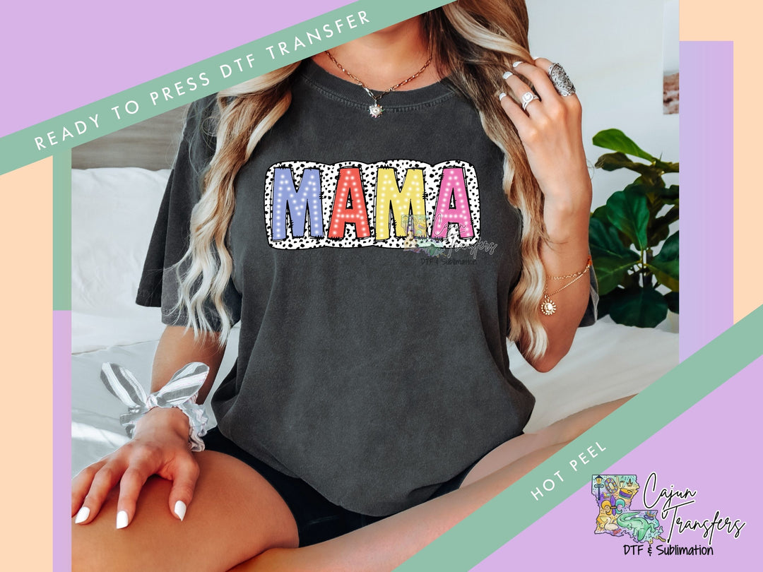 a woman sitting on a bed wearing a black shirt with the word mama on it
