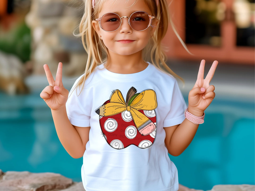 a little girl wearing a shirt with an apple on it