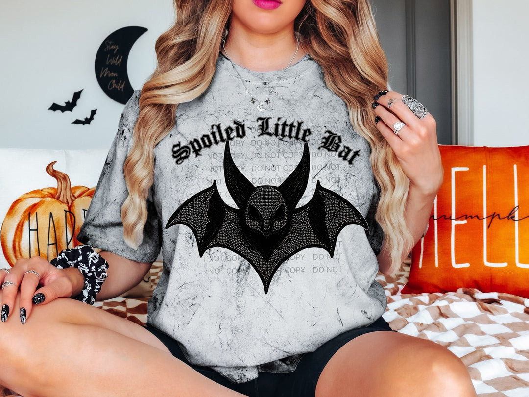 a woman sitting on a bed wearing a shirt with a bat on it