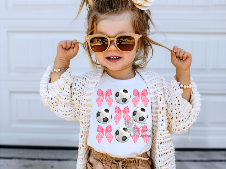 a little girl wearing sunglasses and a t - shirt with soccer balls on it